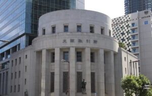 Round, neoclassical stone building with tall pillars and a statue in front, in a modern city street.