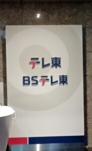 Signboard with テレ東 and BSテレ東 logos in blue and red on a white background with concentric circles design at the center.