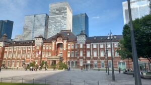 Red brick historic building in front of tall glass skyscrapers in a spacious city square, with people walking around.